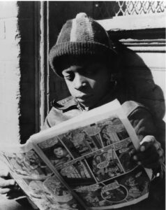 Black and white picture of an african american boy reading a comic book